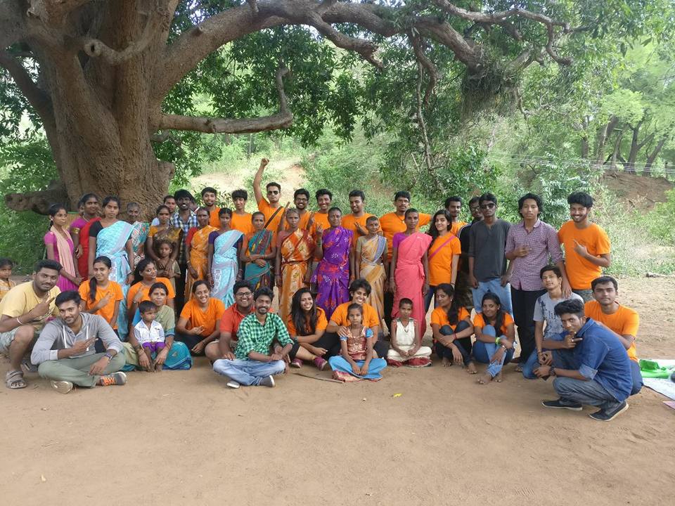 Prayag volunteers and community members gathered outdoors under a large tree